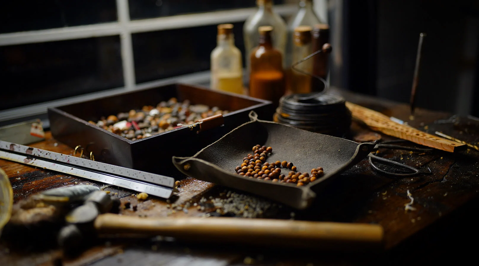 The Cypress Pebble workbench: trays of beads, corked bottles, a steel rule and a hammer under window light