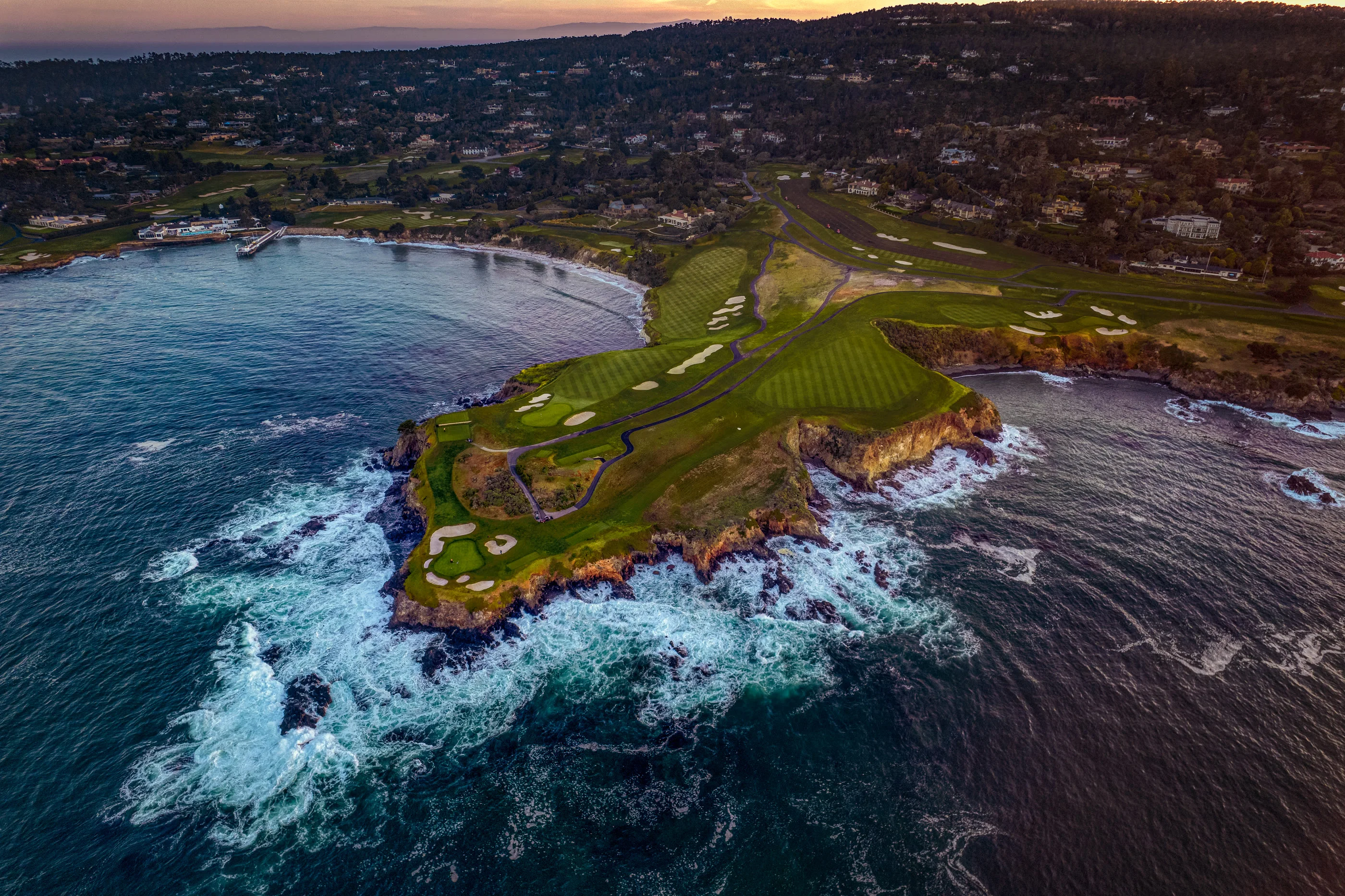 Dusk aerial of the Monterey coast: fairways and bunkers meeting dark ocean and breaking surf